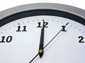 Close up of the top of an analogue clock, showing time as five seconds past twelve.