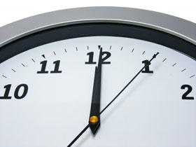 Close up of the top of an analogue clock, showing time as five seconds past twelve.